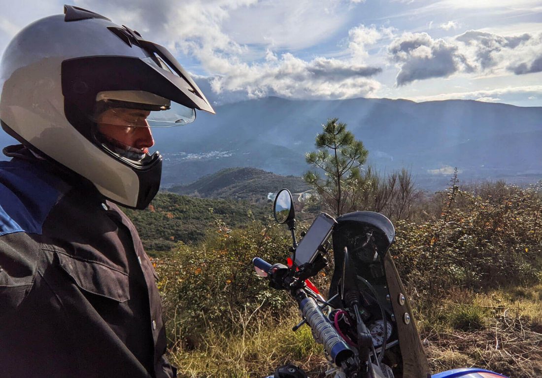 Motorista y moto de perfil con la montaña y rayos de sol al fondo
