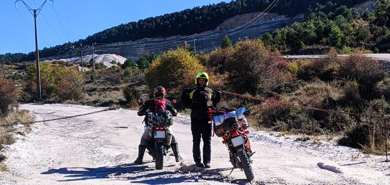 Un piloto levantando una cadena mientras otro pasa con su moto por debajo