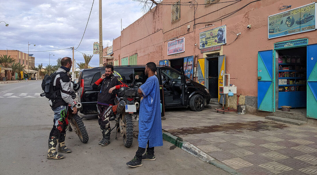 Dos motoristas hablando con un local marroquí a la entrada de un taller.