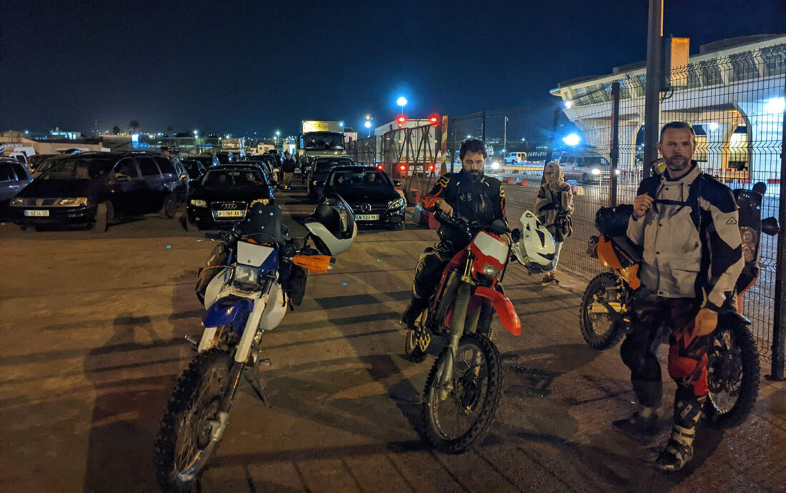 Tres motos y dos moteros de noche en el aparcamiento del ferry